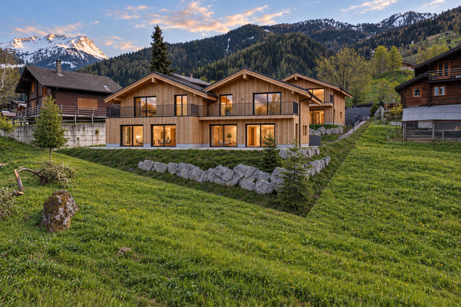 Image de synthèse : les deux bâtiments en bois vus depuis le pré en contrebas, enrochement et sapins, montagnes derrière.